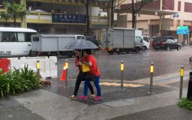 Two women sharing an umbrella during torrential afternoon storm.