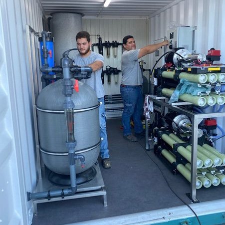 Foto da equipe Elemental Water Makers e parceiros com alguns equipamentos para uma solução de dessalinização de água do mar movida a energia solar fora da rede. Foto: Fabricantes de Água Elemental.