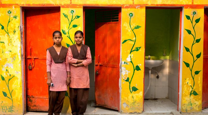 Two girls in front of a toilet facility in India