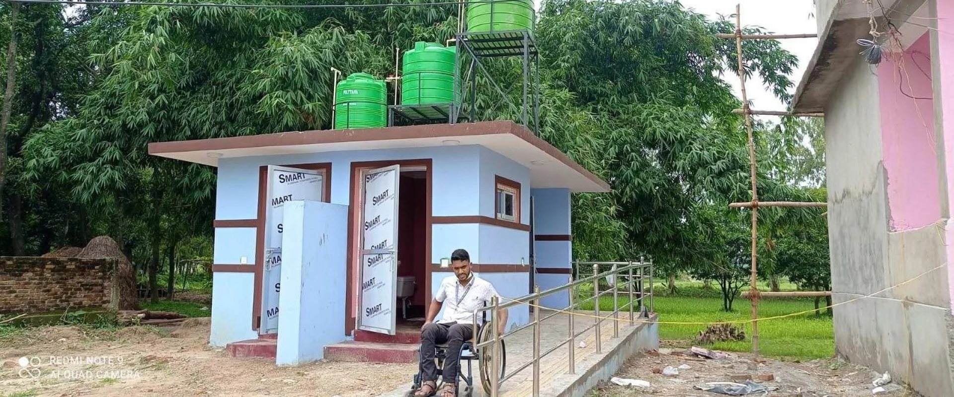 Disable person in front of health care centre in Nepal with a user's friendly toilet.