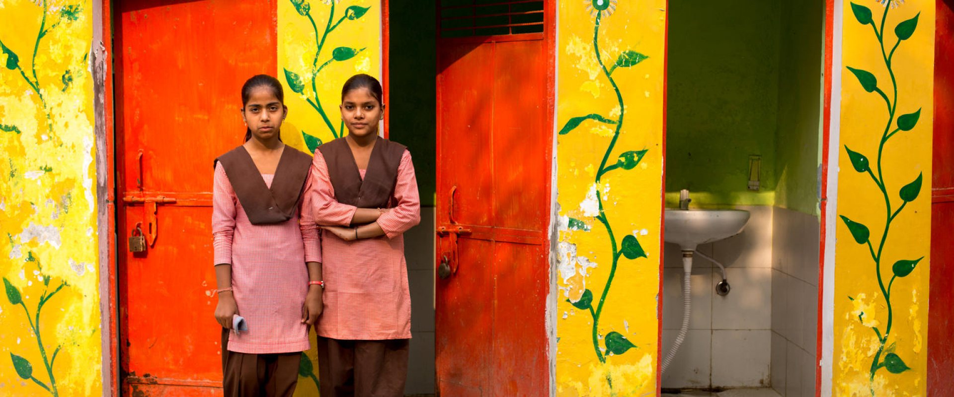 Two girls in front of a toilet facility in India
